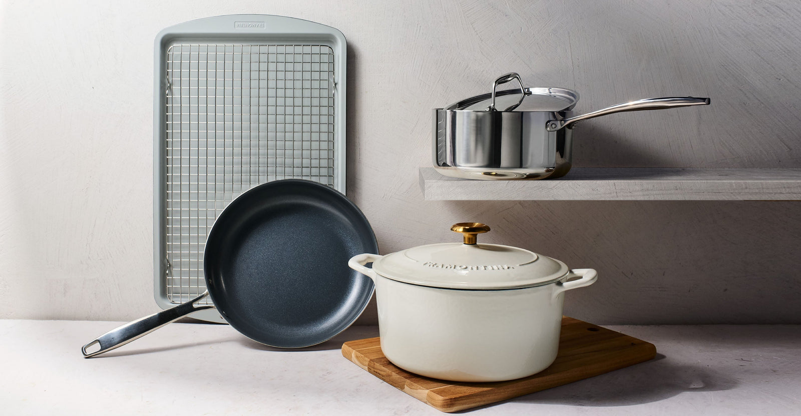 essential cookware set for a first kitchen, featuring a Dutch oven, nonstick skillet, saucepan, and sheet pan arranged neatly on a kitchen counter.