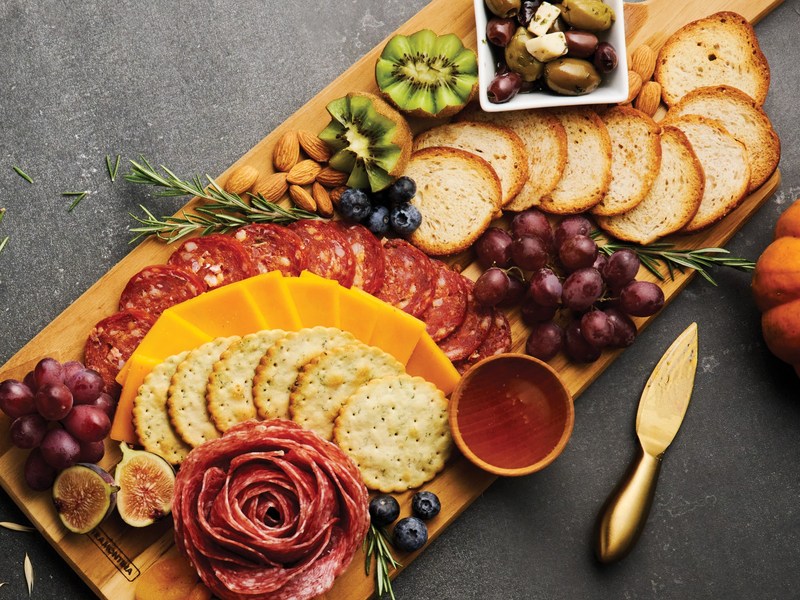 Charcuterie board ideas: a Tramontina teak serving board with salami, cheddar, crackers, grapes, figs, and olives