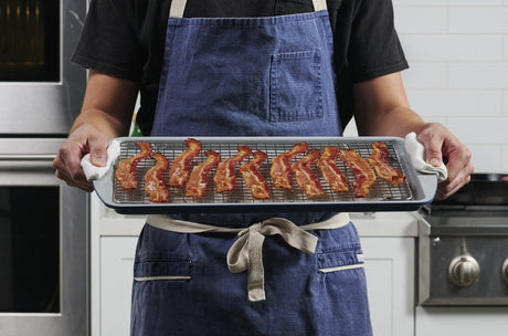 How to cook bacon in the oven with Tramontina sheet pan lined with a wire rack holding crisp strips of oven-cooked bacon, carried fresh from the oven