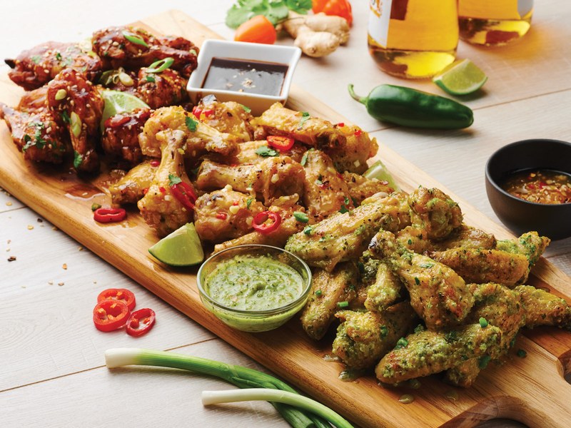 Game day food: three styles of sauced chicken wings with dipping sauces on a Tramontina teak serving board