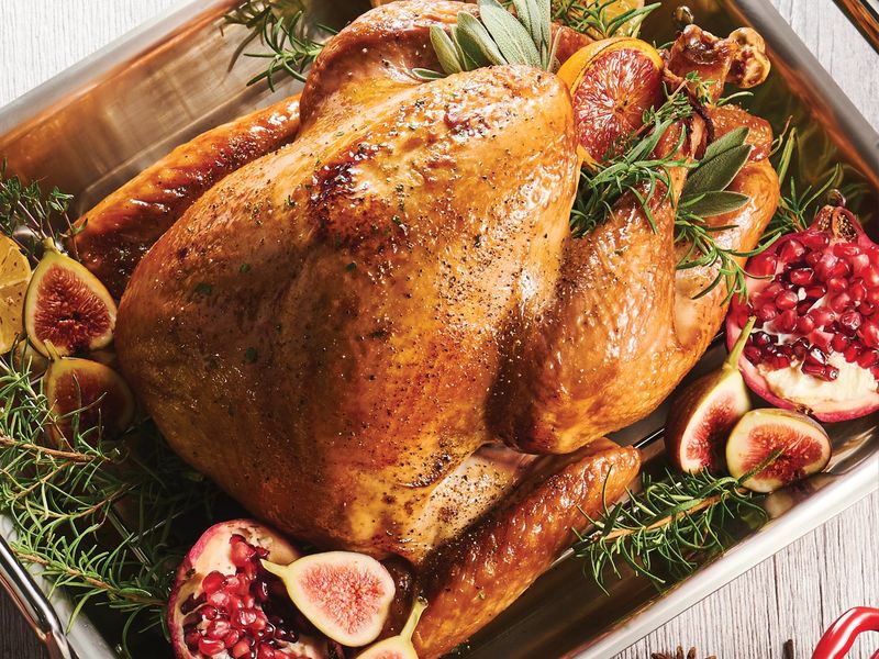 What temperature to cook a turkey: a whole roasted turkey browned deep golden with sage on the V-rack of a Tramontina stainless steel roasting pan.
